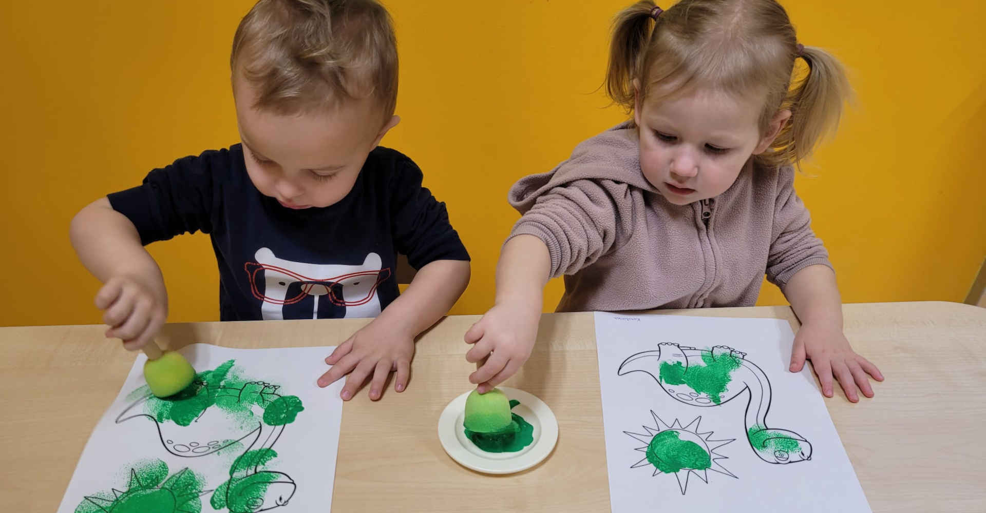 Dziewczynka z chłopcem malują zielone dinozaury